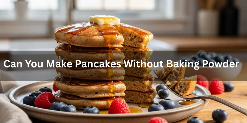 A stack of pancakes topped with butter and syrup sits on a plate surrounded by blueberries and raspberries. A fork is lifting a bite. Text overlay asks, "Can You Make Pancakes Without Baking Powder?"-can you make pancakes without baking powder
