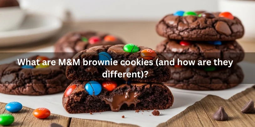 Fudgy brownie-style cookies with crackly tops and colorful candy-coated chocolate pieces, stacked on parchment with a broken cookie showing a gooey chocolate center.-m&m brownie cookies