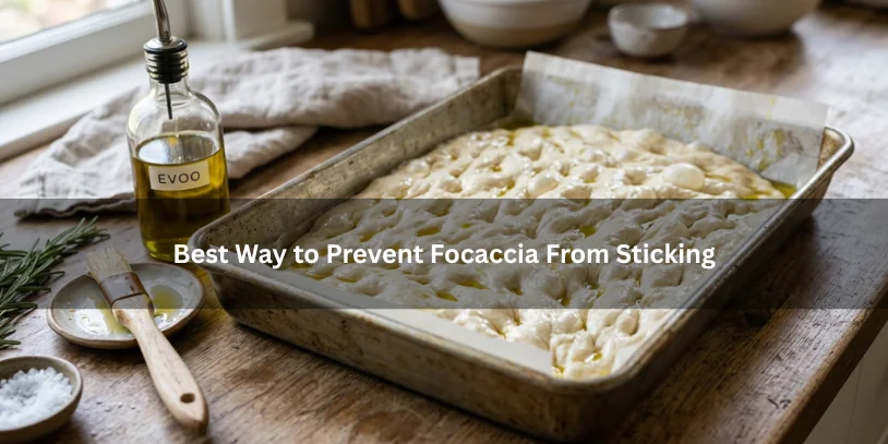 Focaccia in a well-oiled, parchment-lined baking pan beside olive oil and a pastry brush, illustrating how to prevent focaccia from sticking.-focaccia sticking to pan 